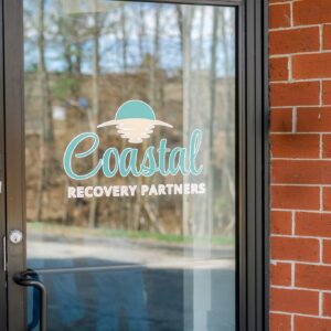 Glass door with the logo and text “Coastal Recovery Partners” beside a red brick wall.