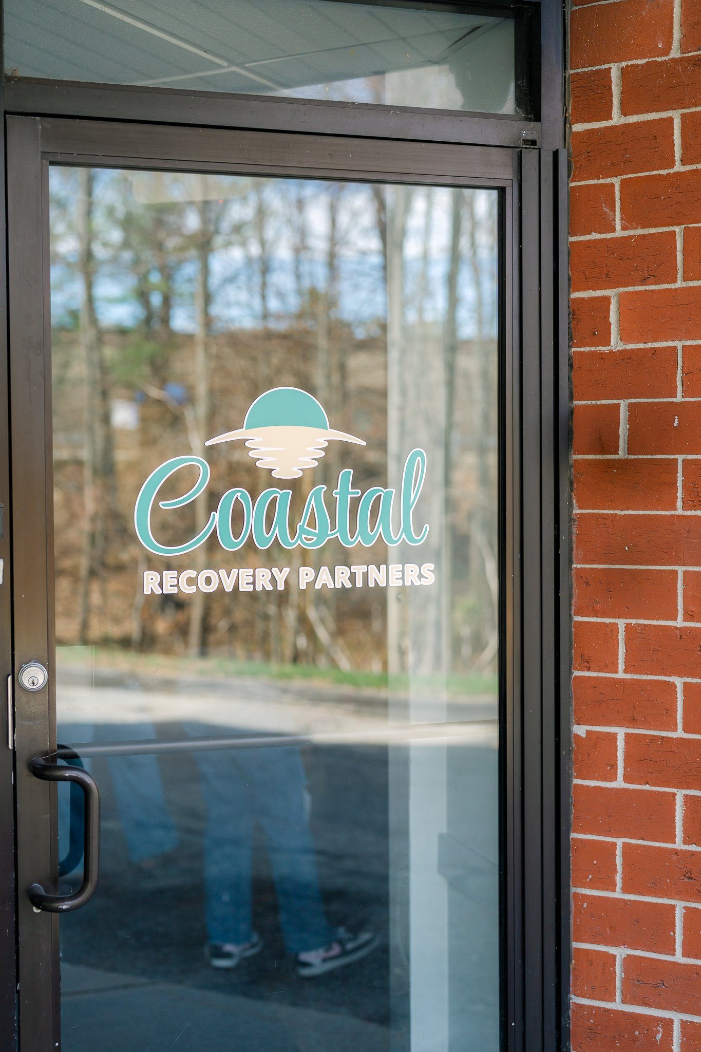 Glass door with the logo and text “Coastal Recovery Partners” beside a red brick wall.
