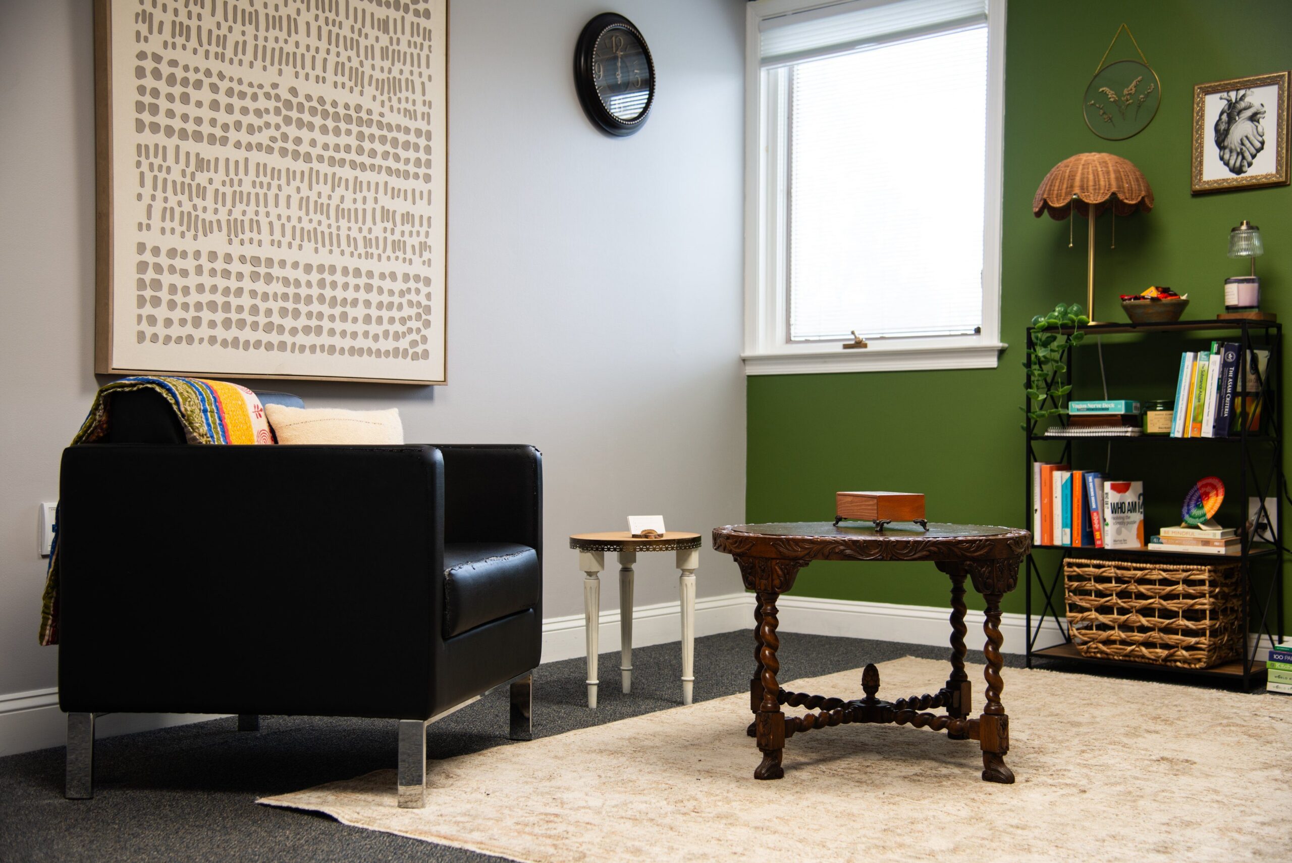 Living room with black armchair, carved wooden table, bookshelf, green accent wall, window, and framed wall art