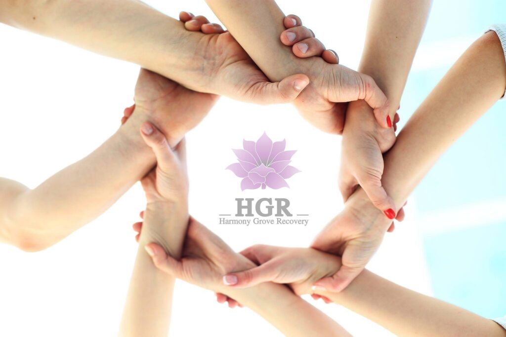 Hands of several people linked in a circle around the HGR Harmony Grove Recovery logo and purple flower.