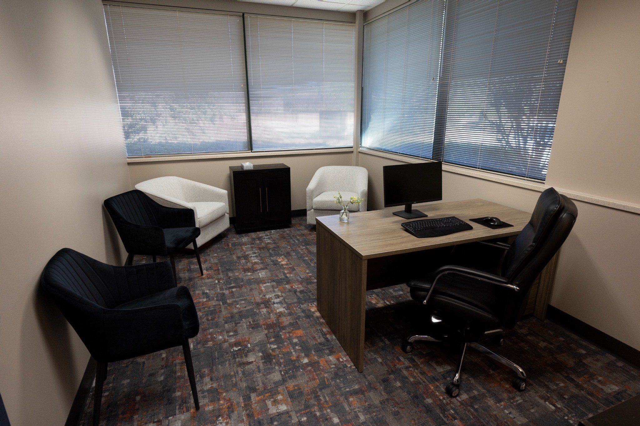 Small office with desk, computer, black chair, two armchairs, and windows with blinds